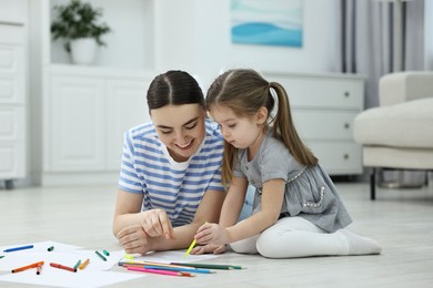 Mother and her little daughter drawing with colorful markers on floor at home