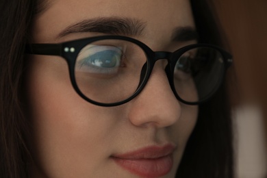 Photo of Beautiful young woman wearing glasses on blurred background, closeup. Ophthalmologist service