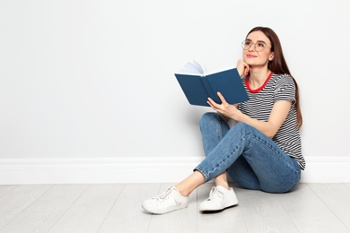 Photo of Young woman reading book on floor near white wall, space for text