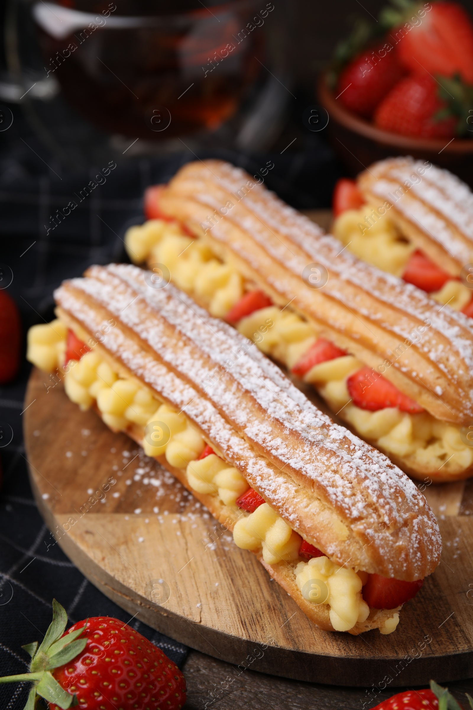 Photo of Delicious eclairs filled with cream and strawberries on table, closeup