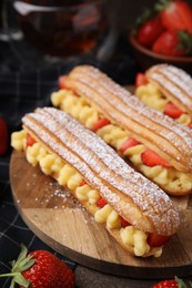 Photo of Delicious eclairs filled with cream and strawberries on table, closeup