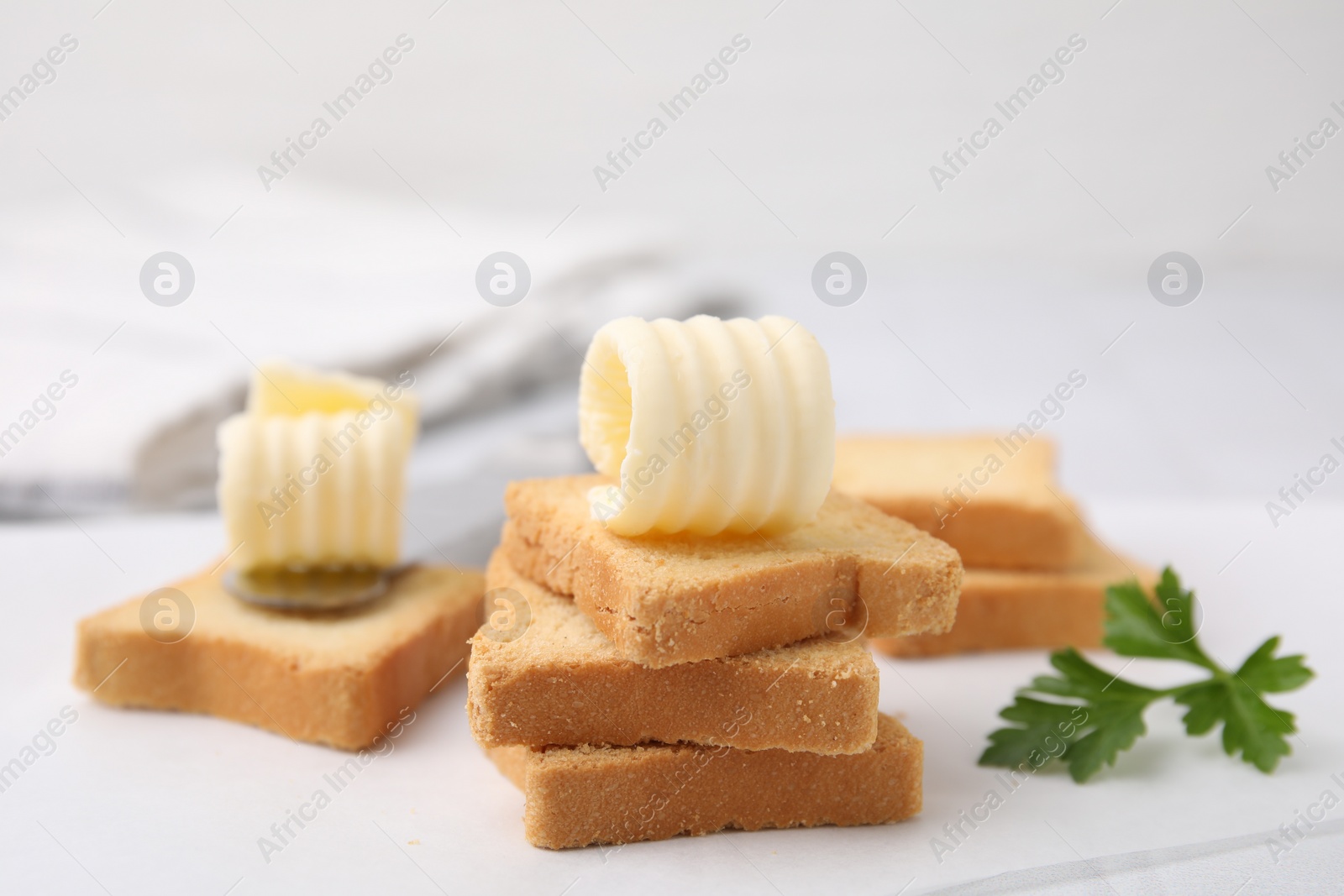 Photo of Tasty butter curls, knife and pieces of dry bread on white table, closeup