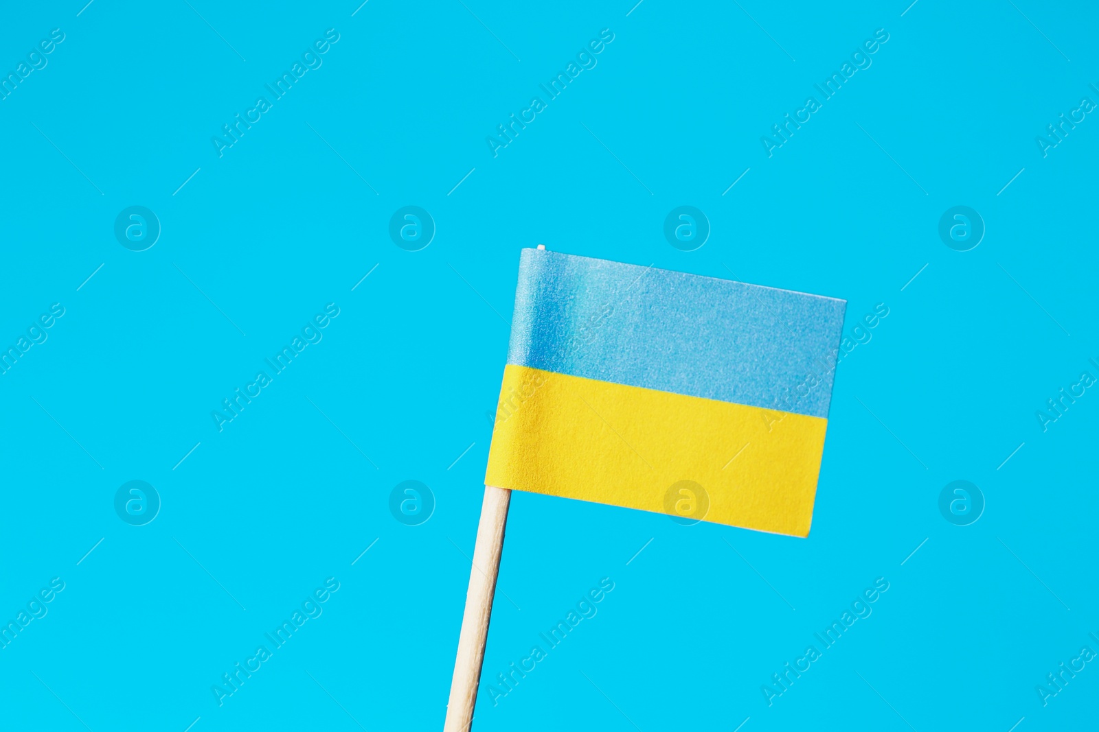 Photo of Small paper flag of Ukraine on light blue background, closeup. Space for text