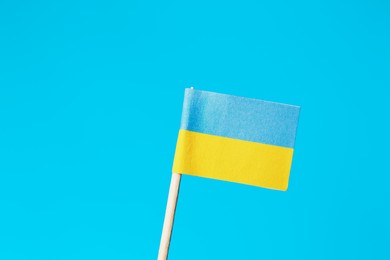 Small paper flag of Ukraine on light blue background, closeup. Space for text