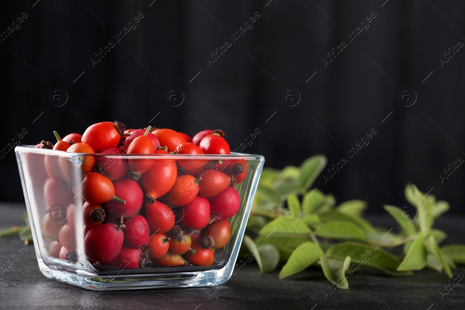 Photo of Ripe rose hip berries with green leaves on black table. Space for text