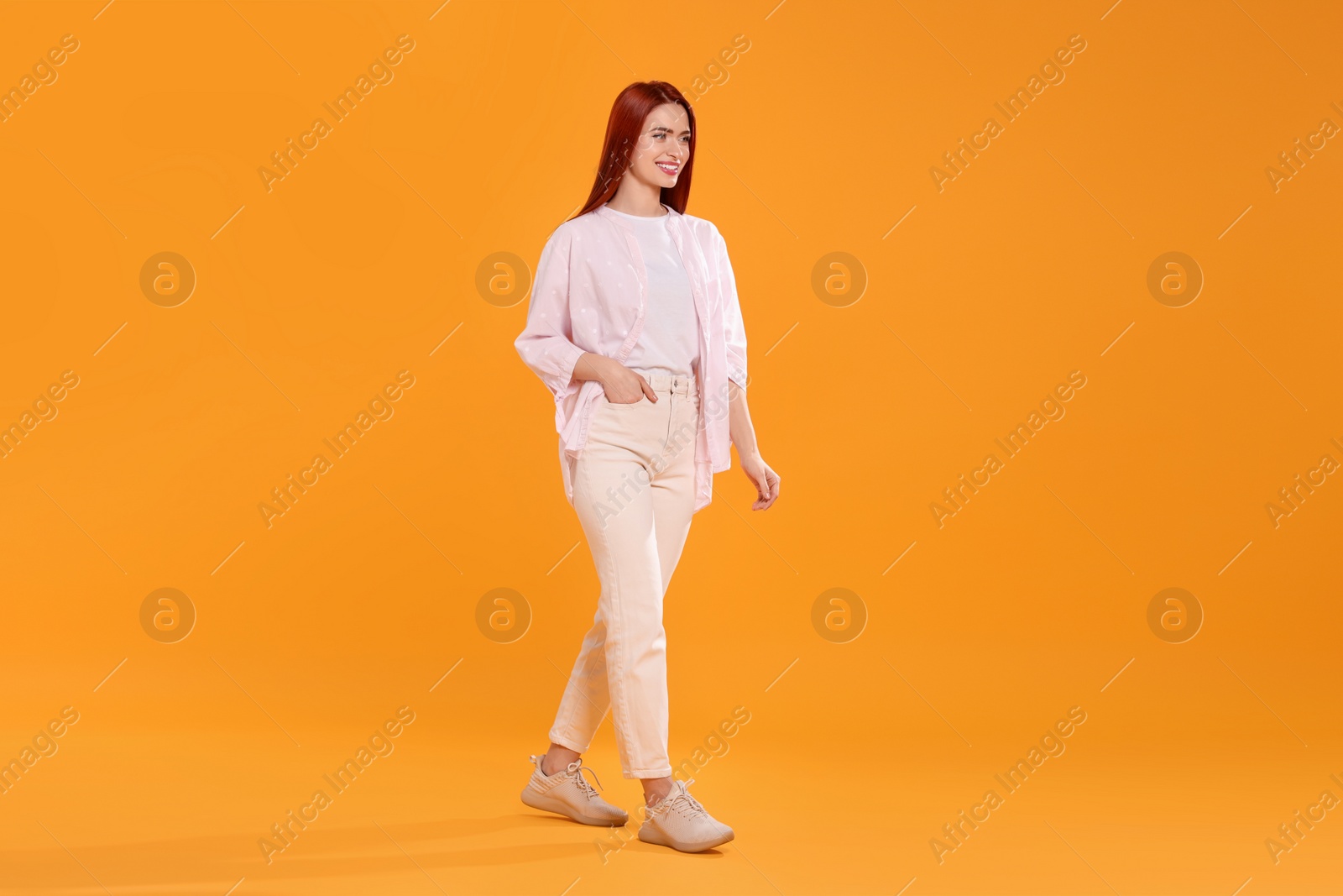 Photo of Happy woman with red dyed hair walking on orange background