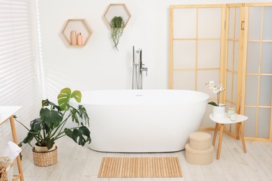 Photo of Stylish bathroom interior with bath tub, houseplants and bamboo mat