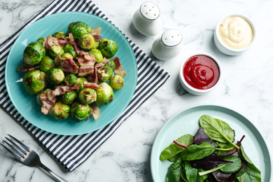 Photo of Delicious Brussels sprouts with bacon on white marble table, flat lay