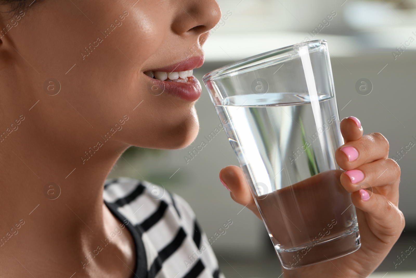 Photo of Young woman drinking water indoors, closeup. Refreshing drink