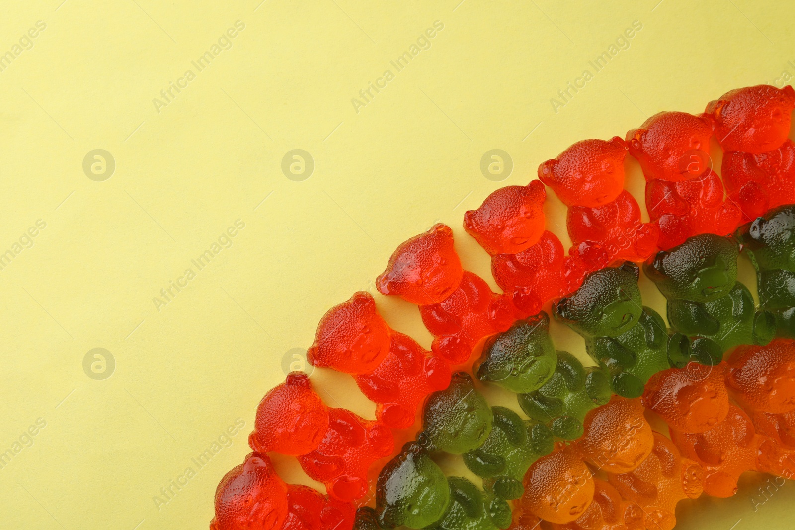 Photo of Different delicious gummy bear candies on yellow background, flat lay. Space for text