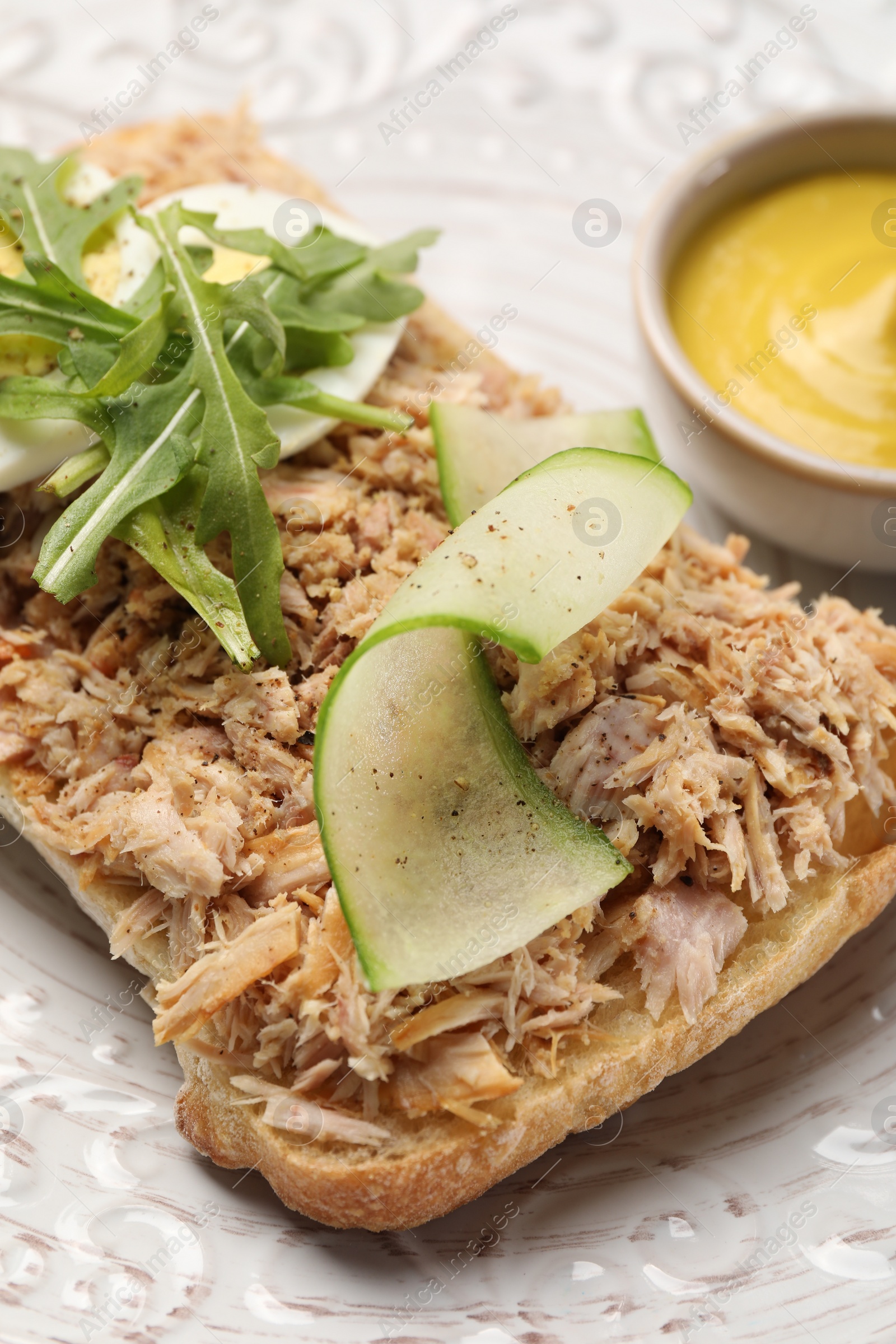 Photo of Delicious sandwich with tuna, boiled egg, vegetables and mustard sauce on white plate, closeup