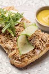 Photo of Delicious sandwich with tuna, boiled egg, vegetables and mustard sauce on white plate, closeup