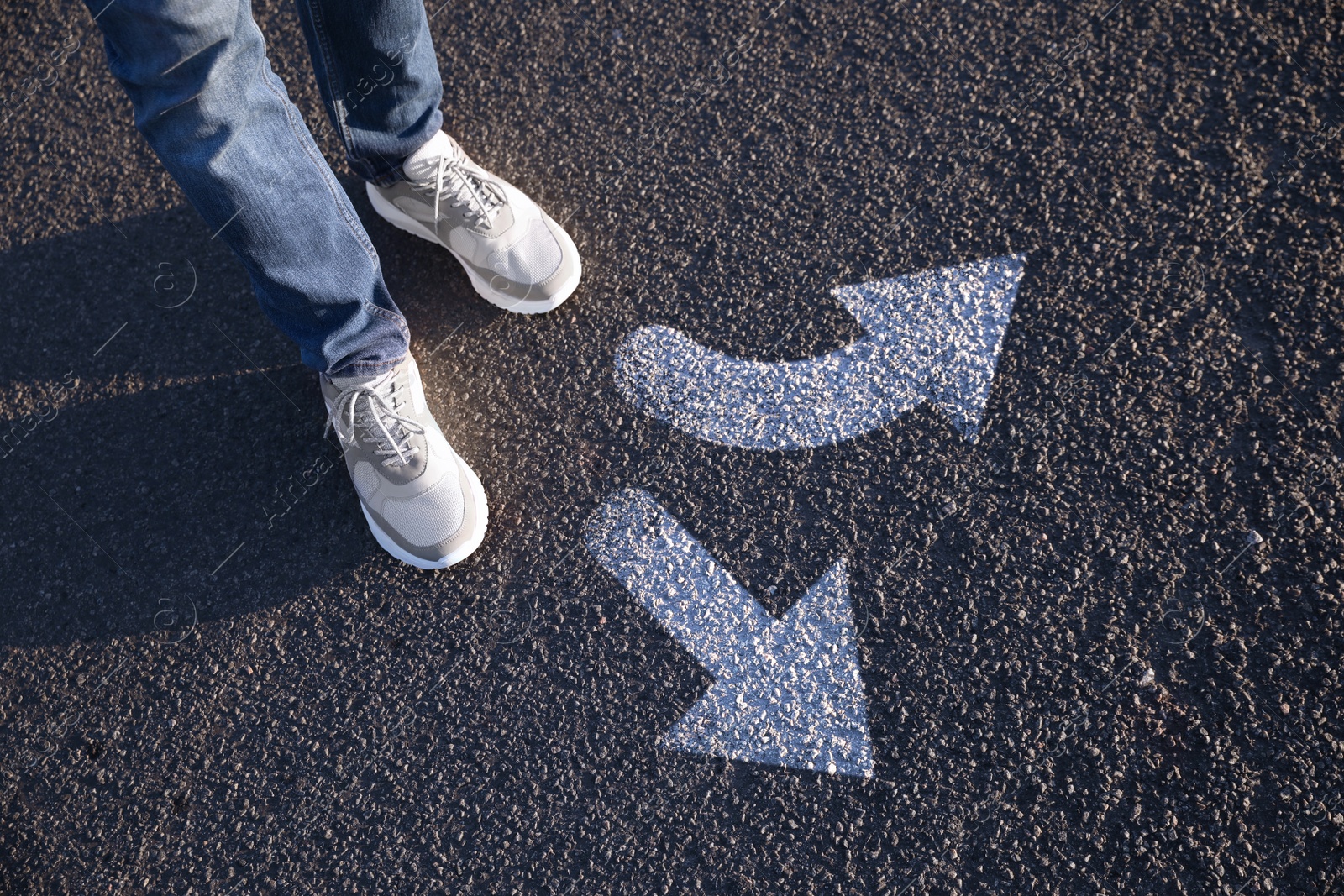 Image of Choice of way. Man standing in front of drawn marks on road, closeup. White arrows pointing in different directions