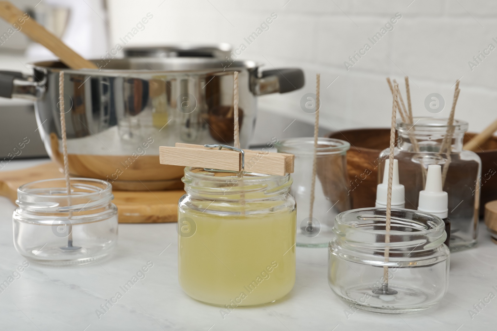 Photo of Glass jar with melted wax and wick on white kitchen table. Making homemade candle