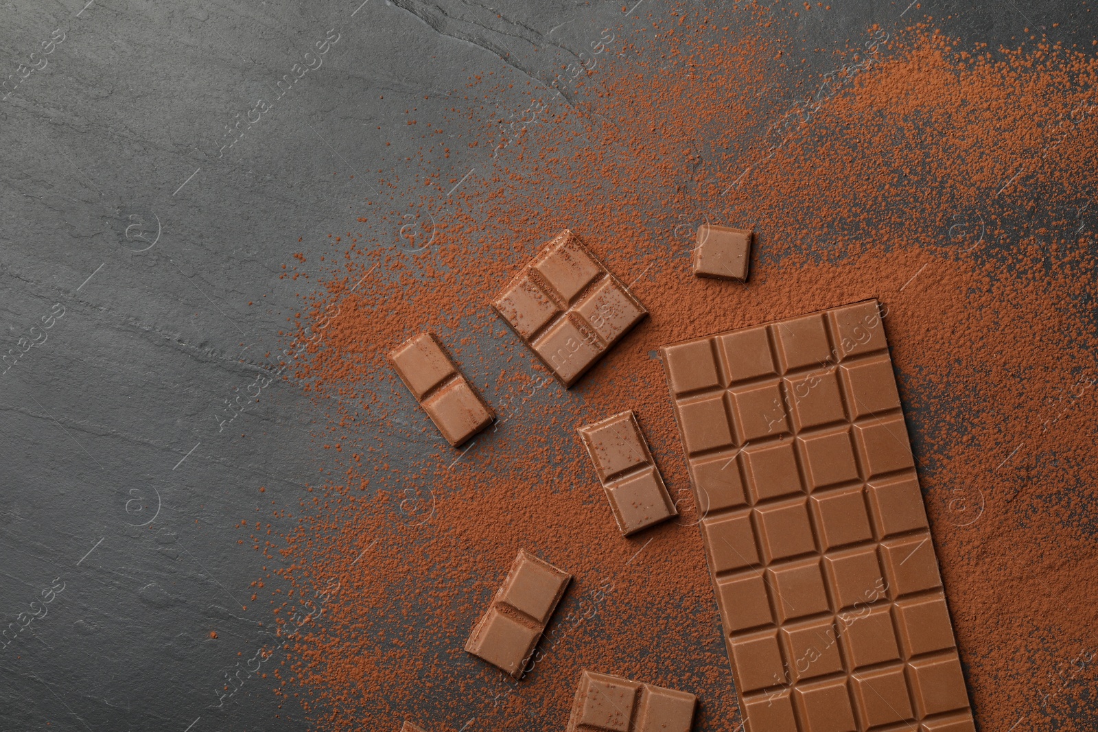 Photo of Pieces of tasty chocolate and cocoa powder on grey table, flat lay. Space for text