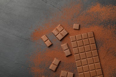 Pieces of tasty chocolate and cocoa powder on grey table, flat lay. Space for text