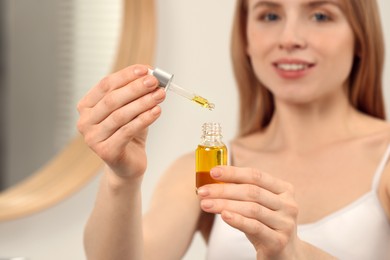 Woman with bottle of essential oil on blurred background, selective focus