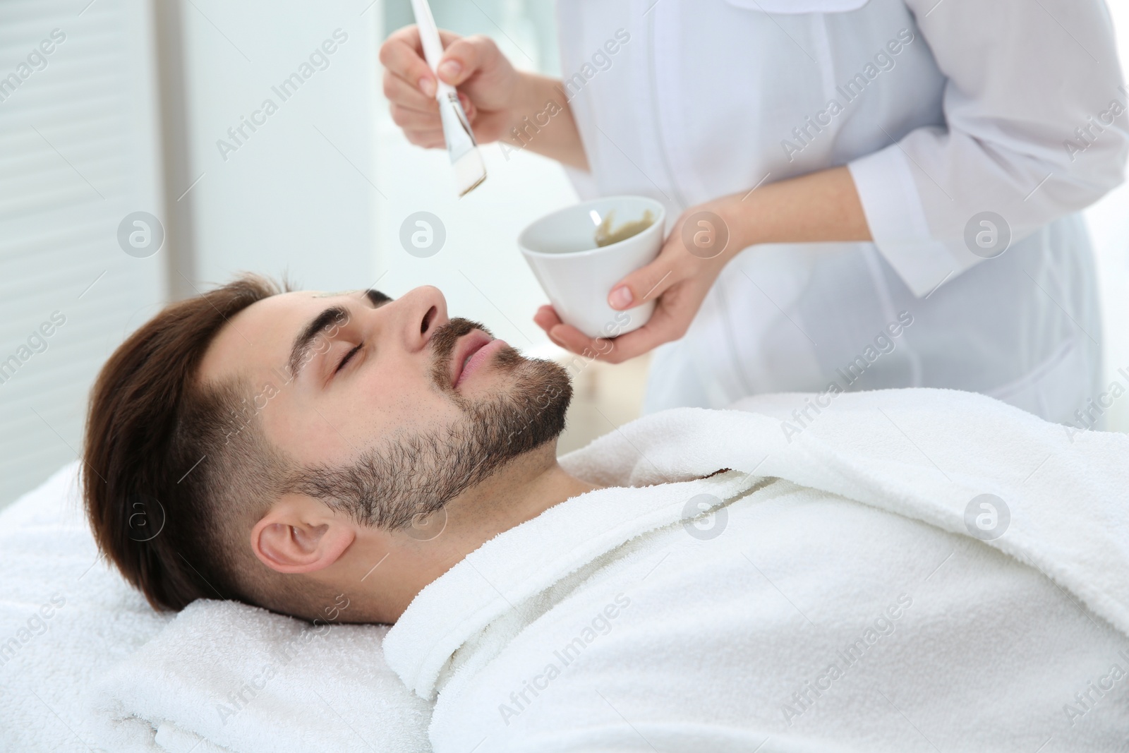 Photo of Cosmetologist applying mask on client's face in spa salon