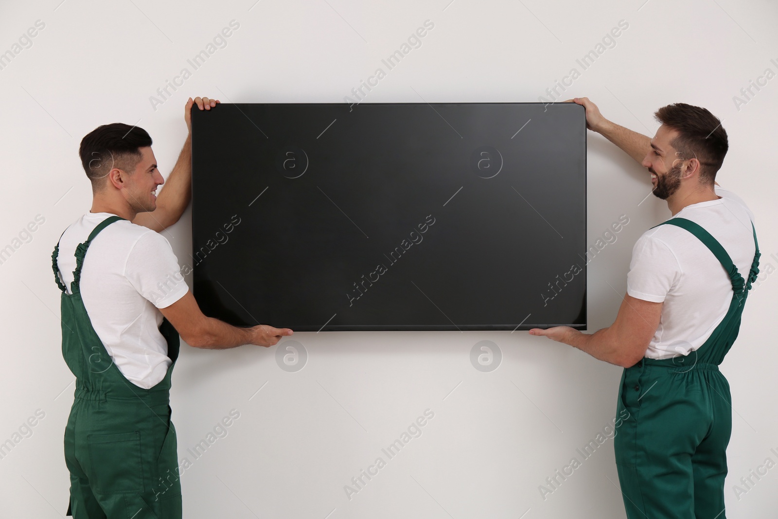 Photo of Professional technicians installing modern flat screen TV on wall indoors