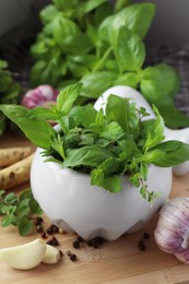 Photo of Mortar with different fresh herbs near garlic, horseradish roots and black peppercorns on wooden table, closeup