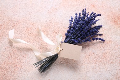 Bouquet of beautiful preserved lavender flowers with blank tag and ribbon on color textured table, top view. Space for text