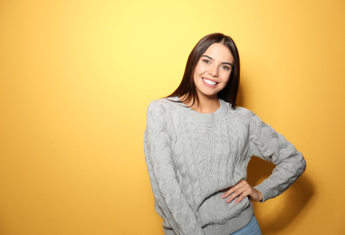 Happy young woman wearing warm sweater on yellow background 