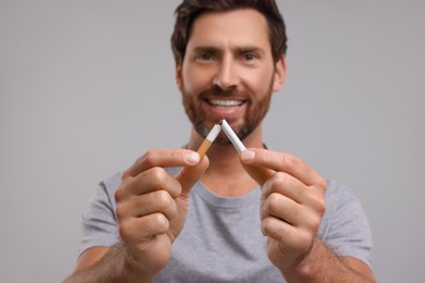 Photo of Stop smoking concept. Smiling man breaking cigarette on grey background, selective focus