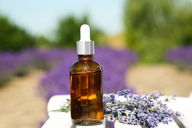 Bottle of essential oil and lavender flowers on white wooden table in field, closeup