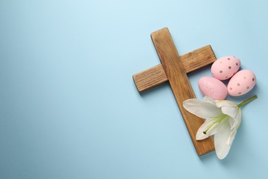 Wooden cross, painted Easter eggs and lily flower on light blue background, top view. Space for text