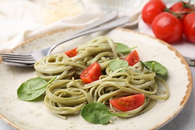 Photo of Tasty pasta with spinach, tomatoes and cutlery on light table, closeup