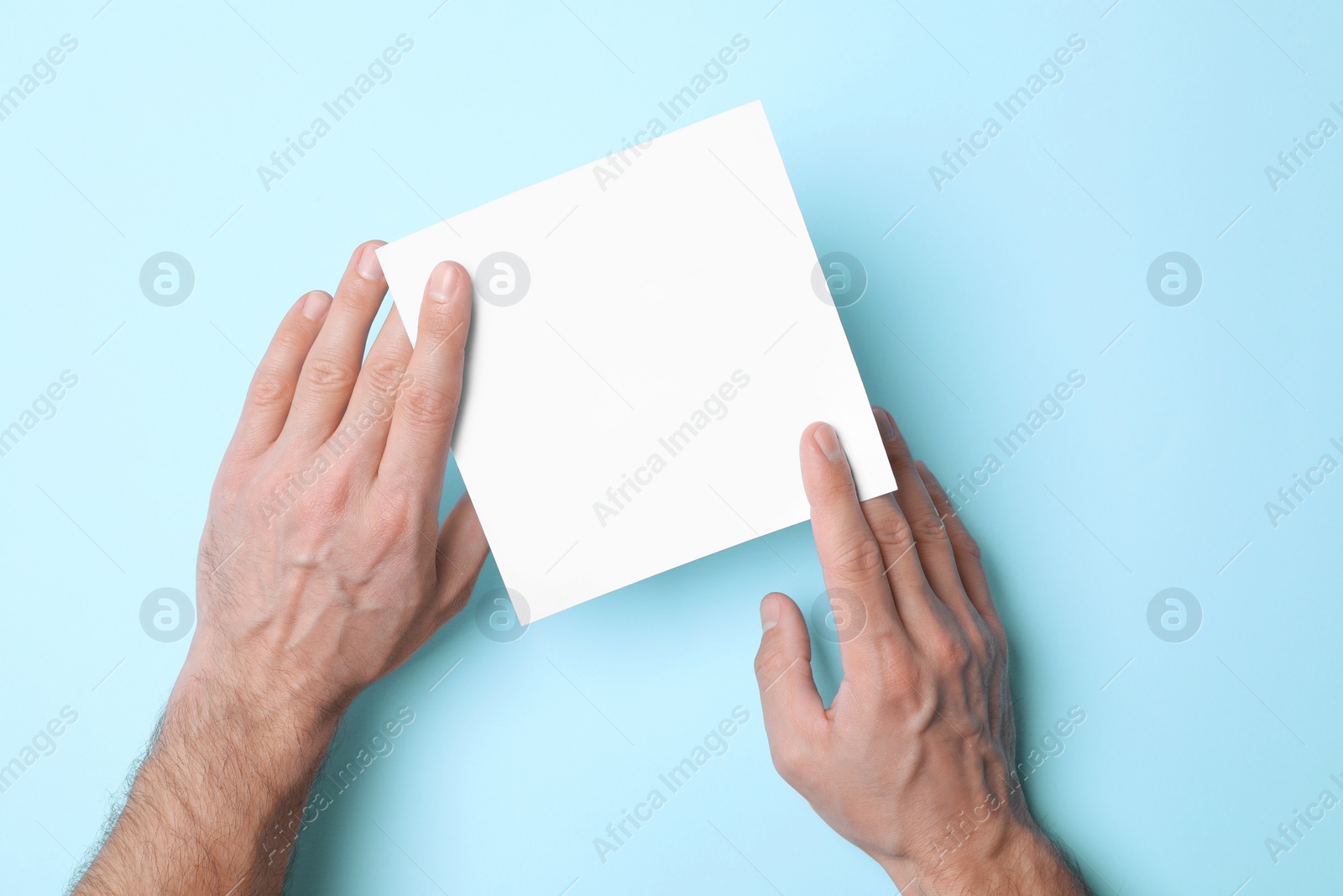 Photo of Man holding sheet of paper on light blue background, top view. Mockup for design