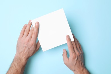 Man holding sheet of paper on light blue background, top view. Mockup for design