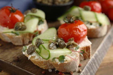 Photo of Bruschettas with capers, vegetables and cream cheese served on wooden board, closeup