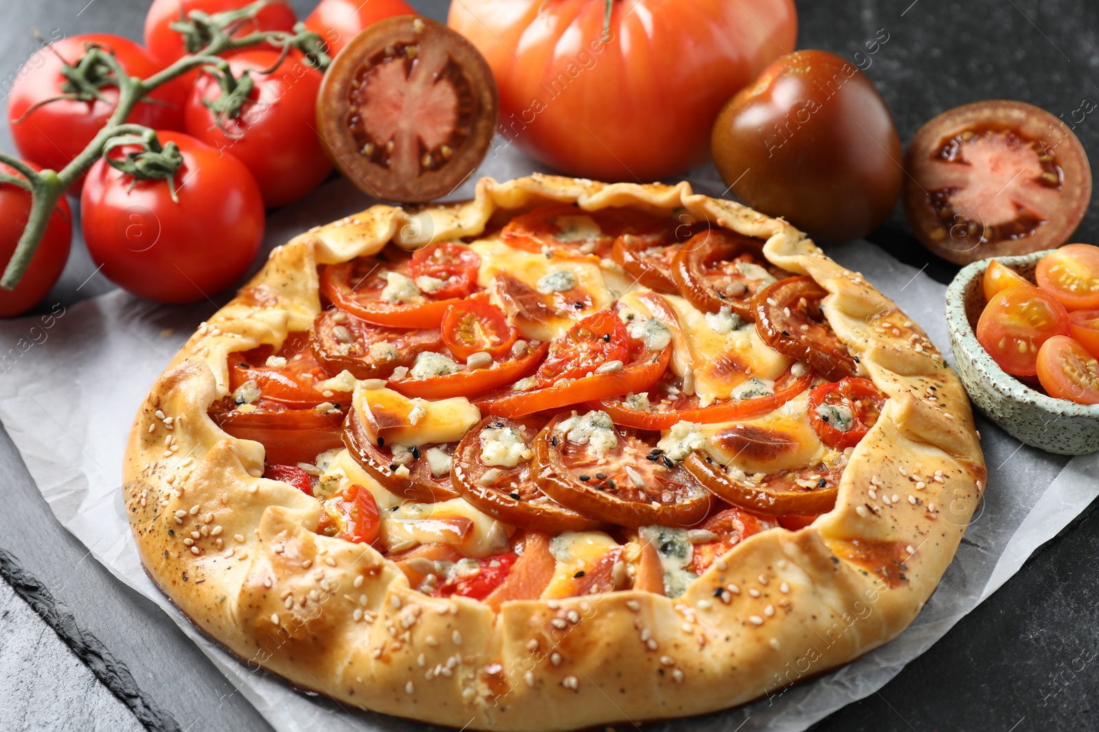 Photo of Tasty galette with tomato and cheese (Caprese galette) on dark table, closeup