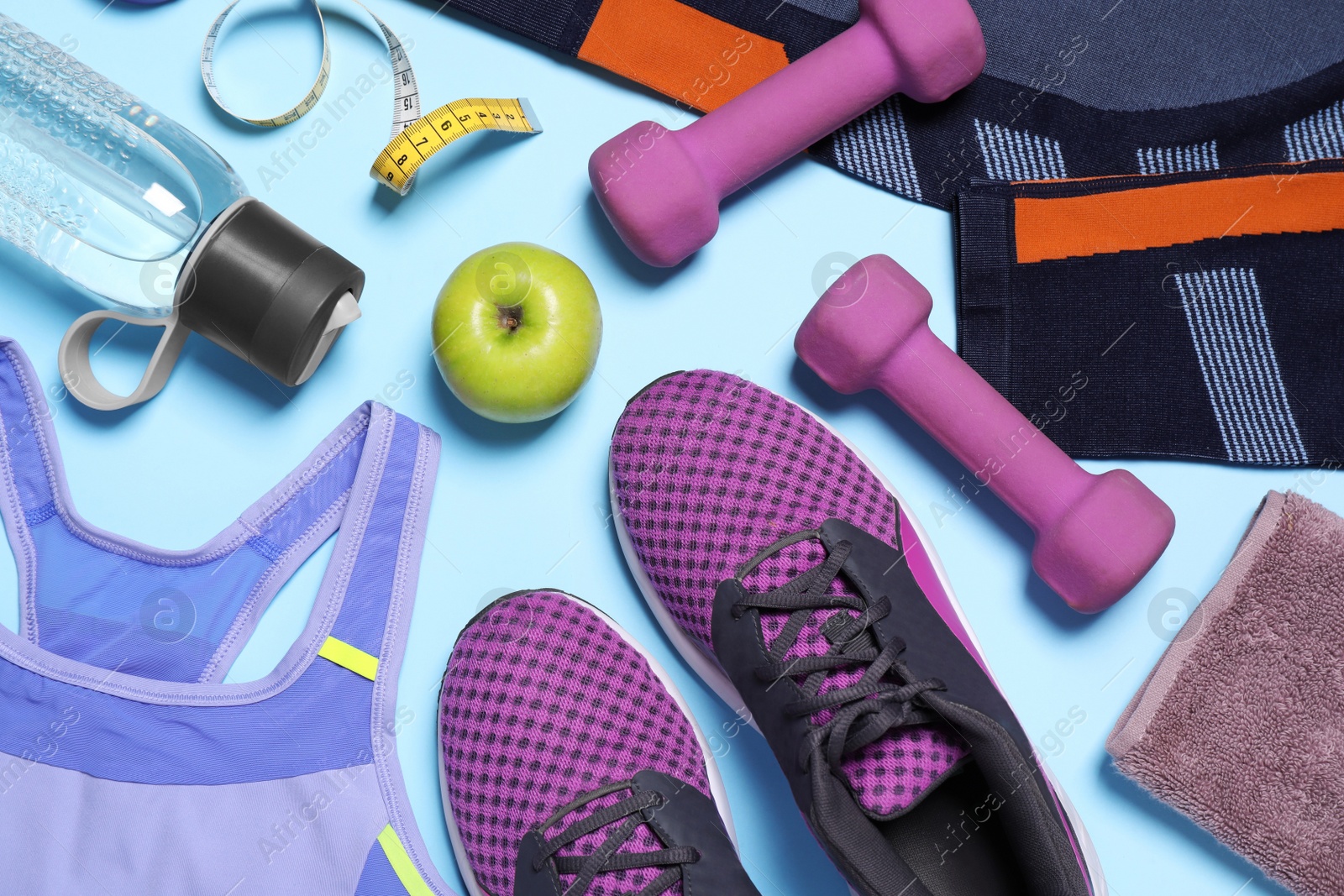 Photo of Flat lay composition with sportswear, sneakers and dumbbells on light blue background