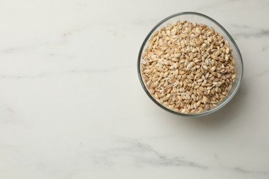 Photo of Dry pearl barley in bowl on white marble table, top view. Space for text