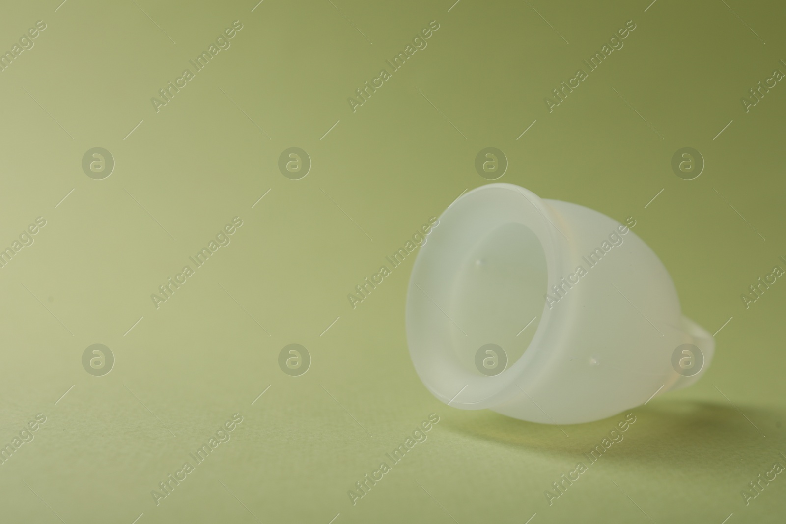 Photo of Menstrual cup on green background, closeup. Space for text