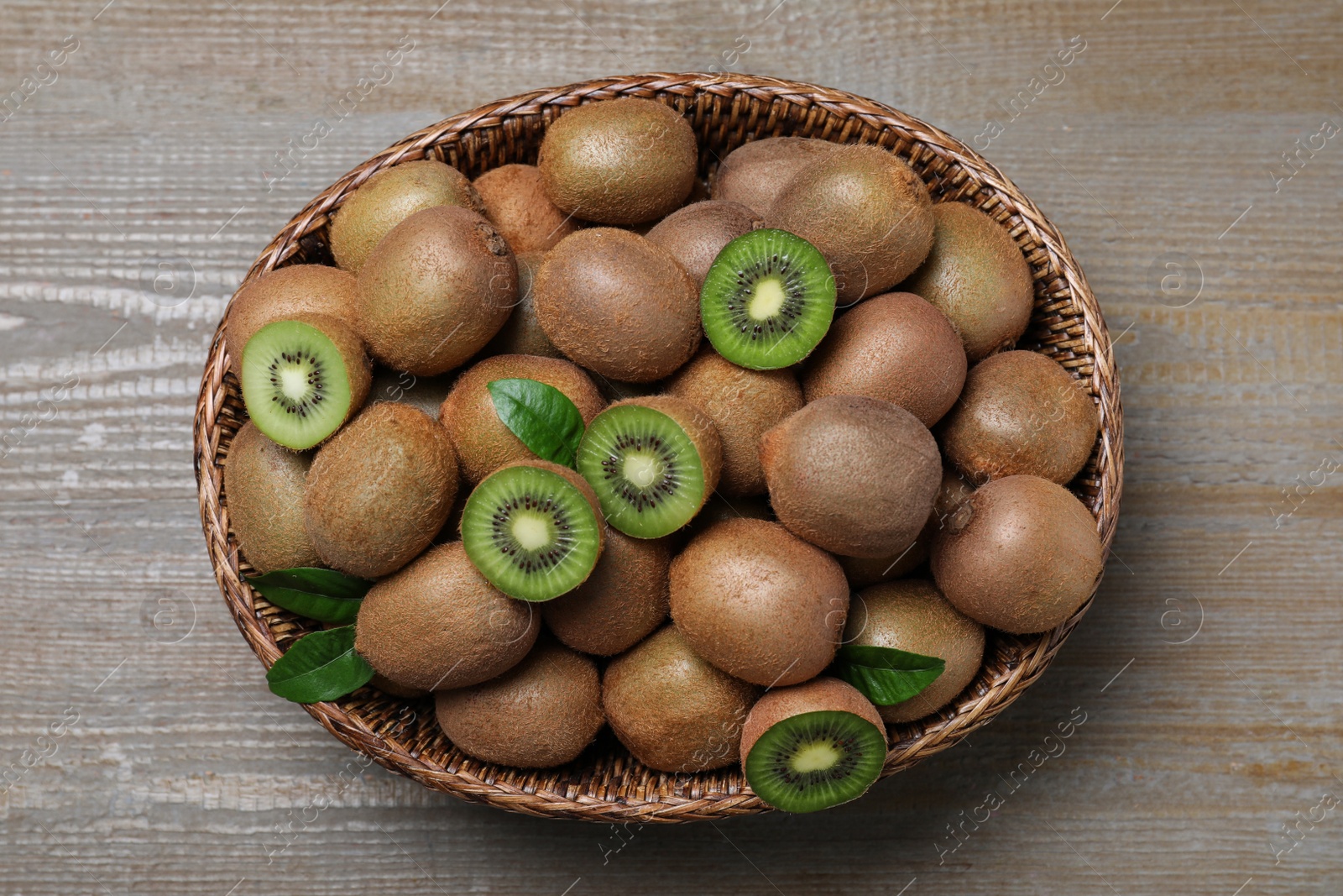 Photo of Fresh ripe kiwis in wicker bowl on wooden table, top view