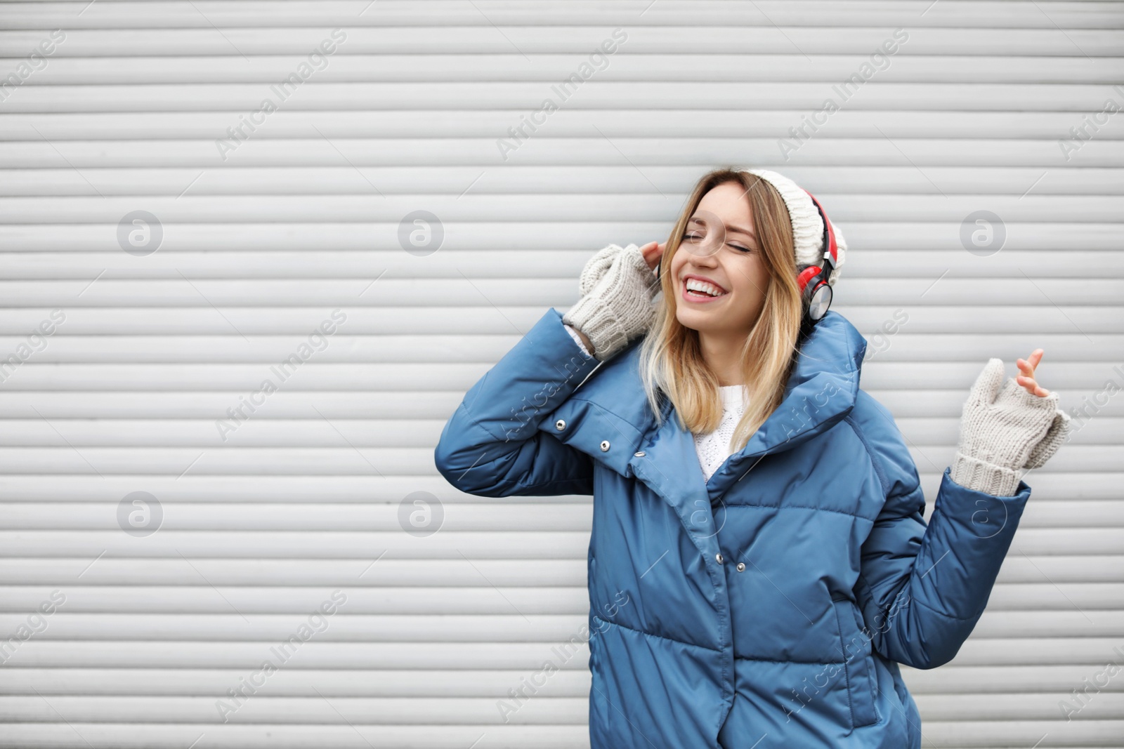 Photo of Young woman with headphones listening to music near light wall. Space for text