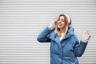 Photo of Young woman with headphones listening to music near light wall. Space for text