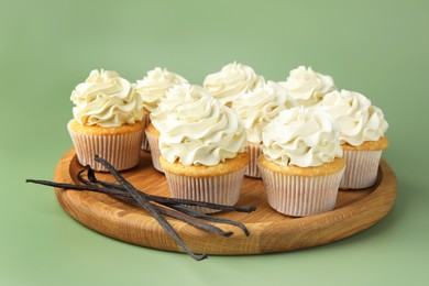 Photo of Tasty cupcakes with cream and vanilla pods on green background