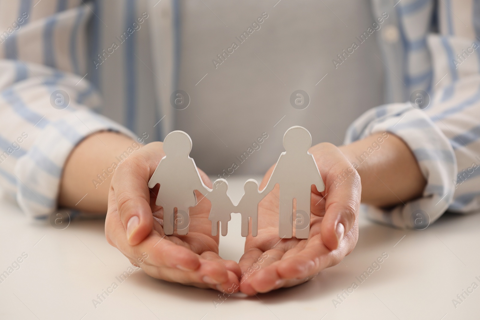 Photo of Woman holding figure of family at white table, closeup