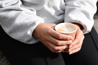 Woman sitting with cardboard cup of coffee, closeup