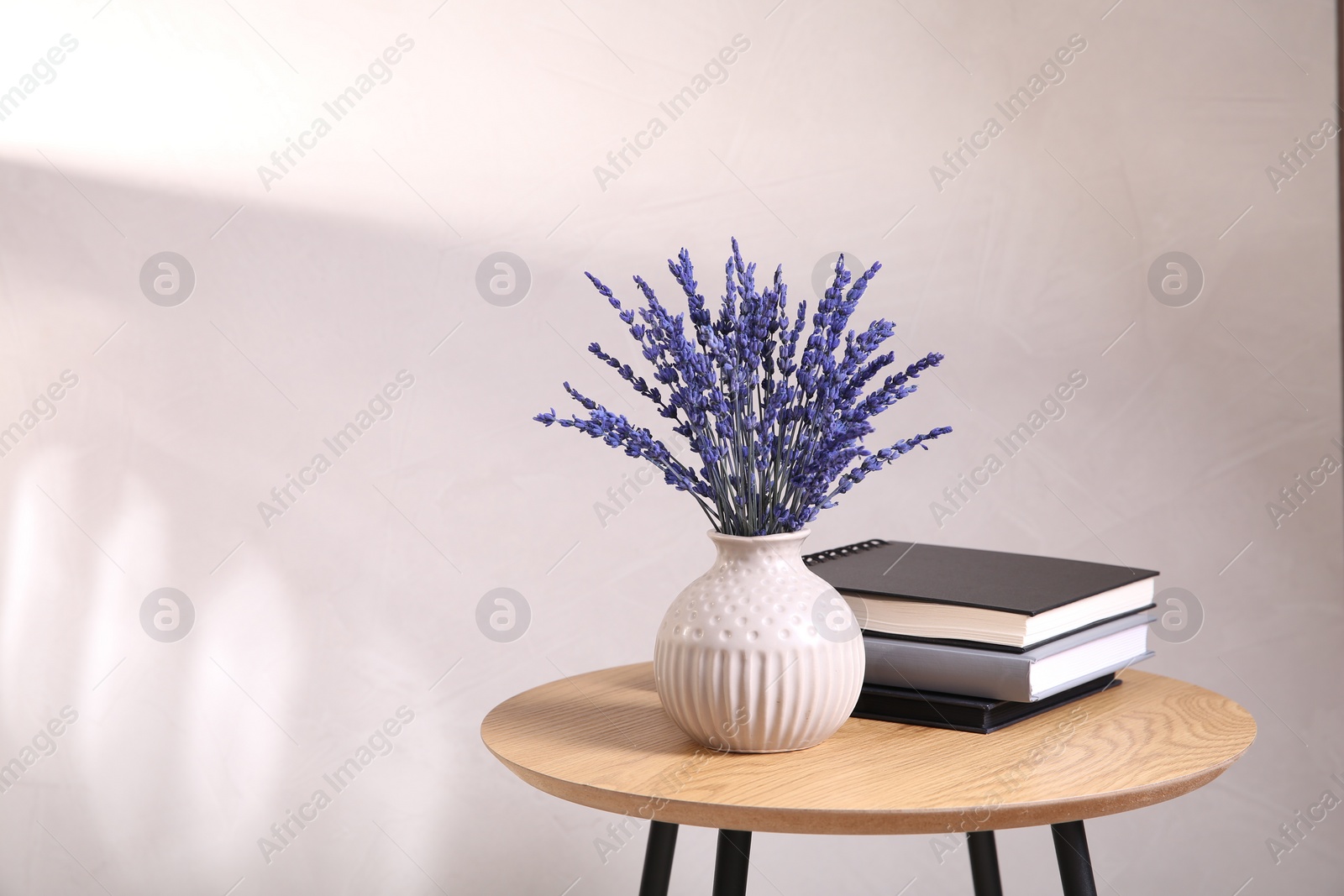 Photo of Bouquet of beautiful preserved lavender flowers and notebooks on wooden table near beige wall, space for text