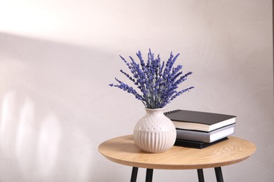 Bouquet of beautiful preserved lavender flowers and notebooks on wooden table near beige wall, space for text