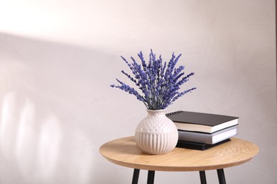 Photo of Bouquet of beautiful preserved lavender flowers and notebooks on wooden table near beige wall, space for text