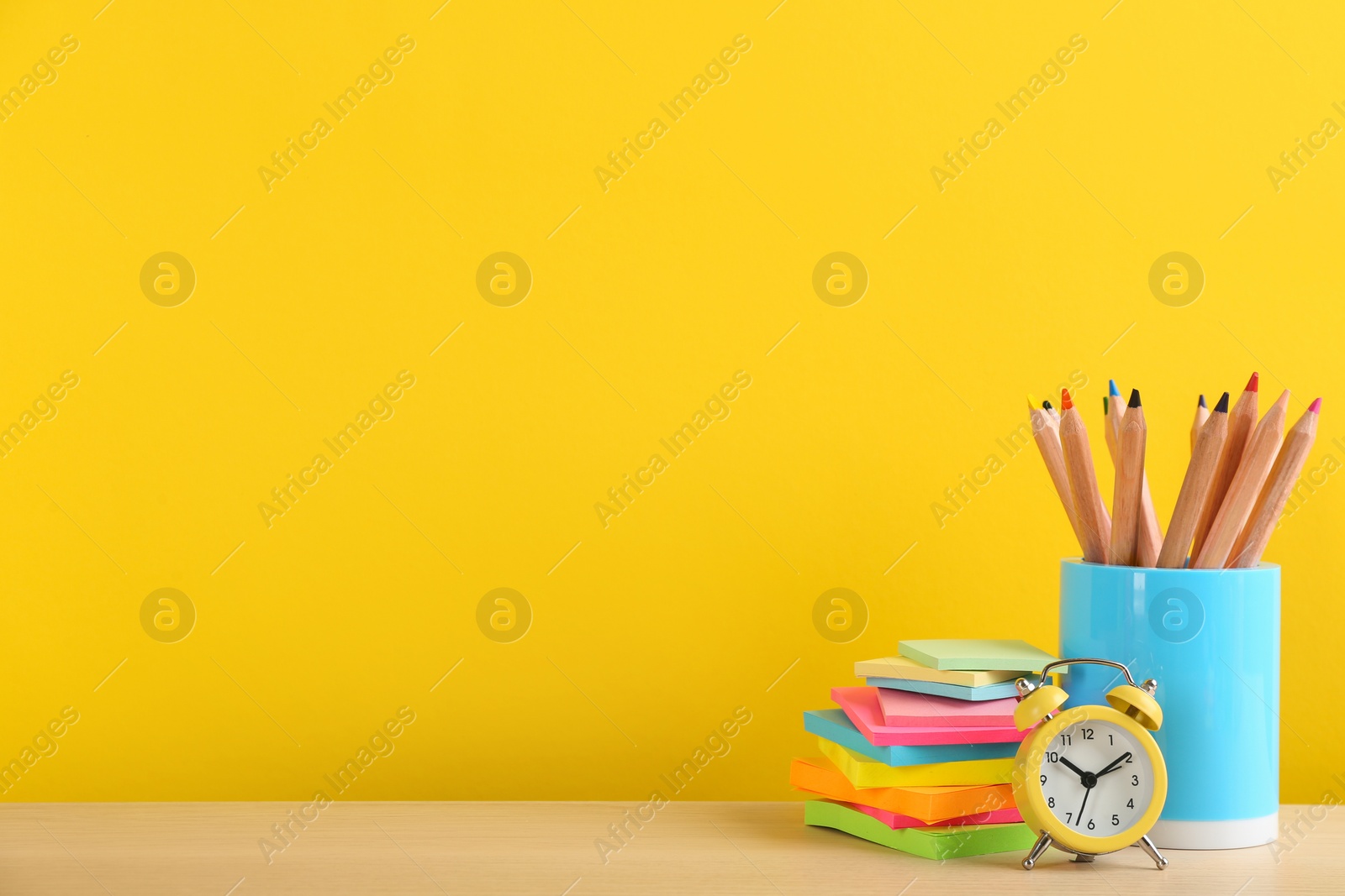 Photo of Different school stationery and alarm clock on table against yellow background, space for text. Back to school