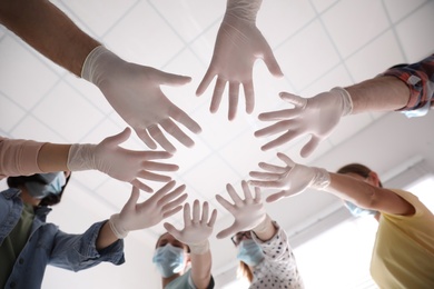 Photo of People in white medical gloves joining hands on light background, low angle view