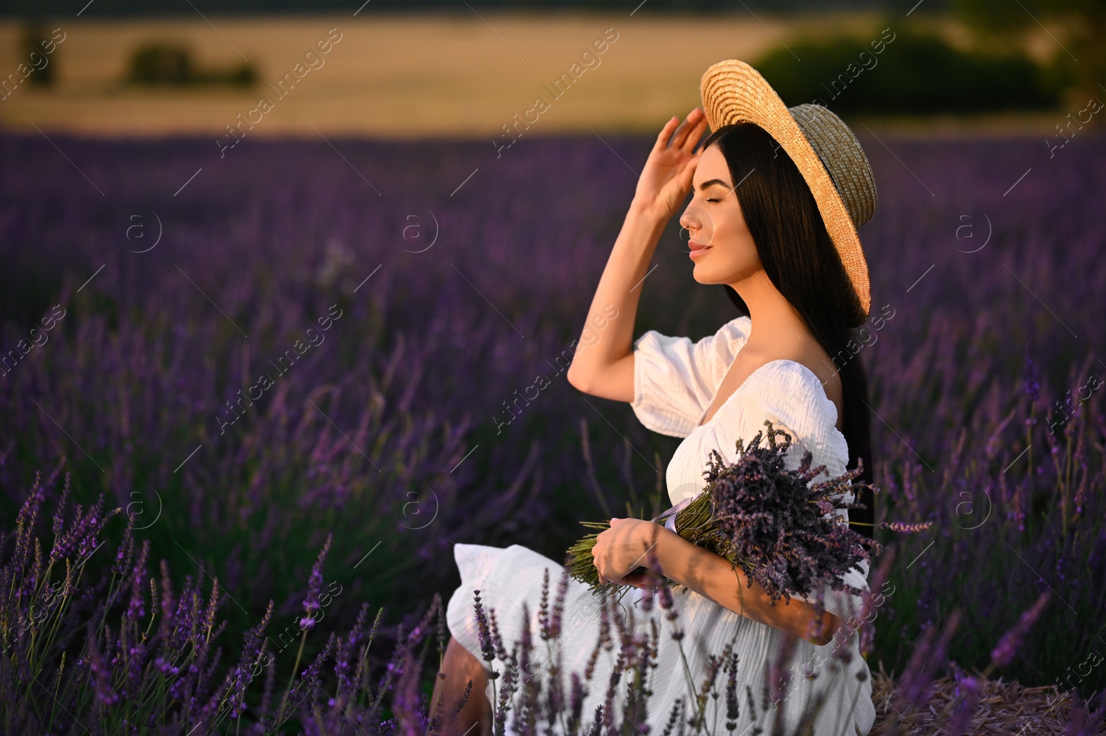 Photo of Beautiful young woman with bouquet sitting in lavender field