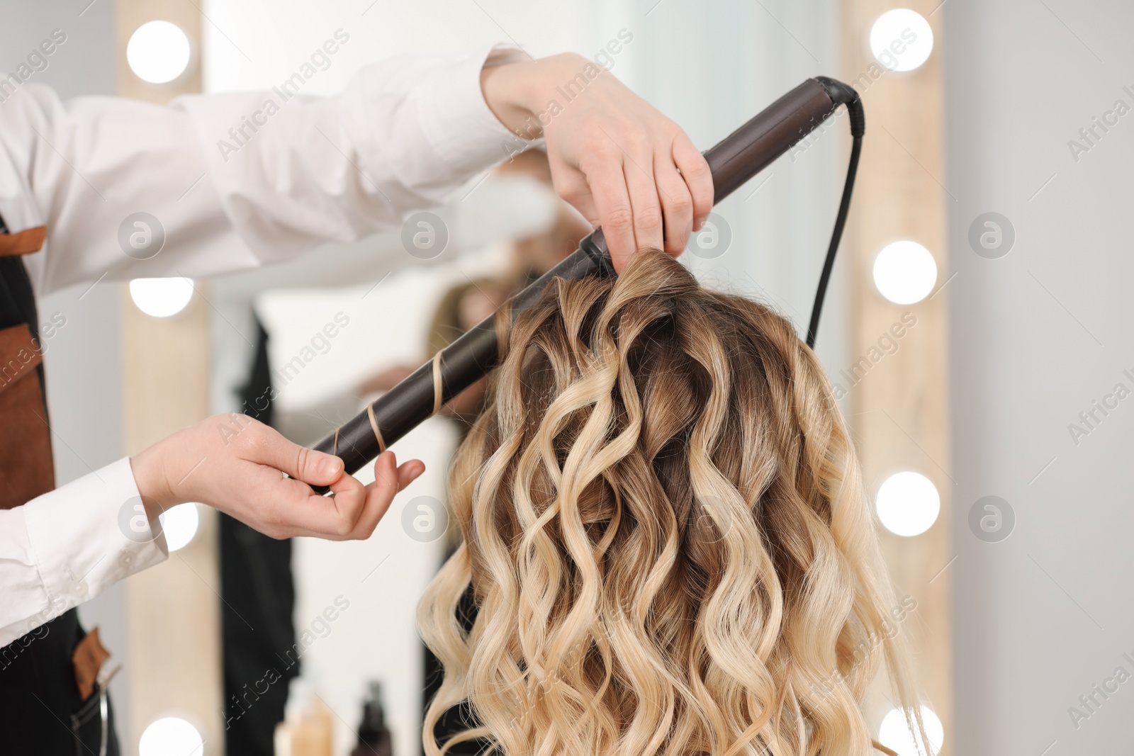 Photo of Hair styling. Hairdresser curling woman's hair in salon, closeup